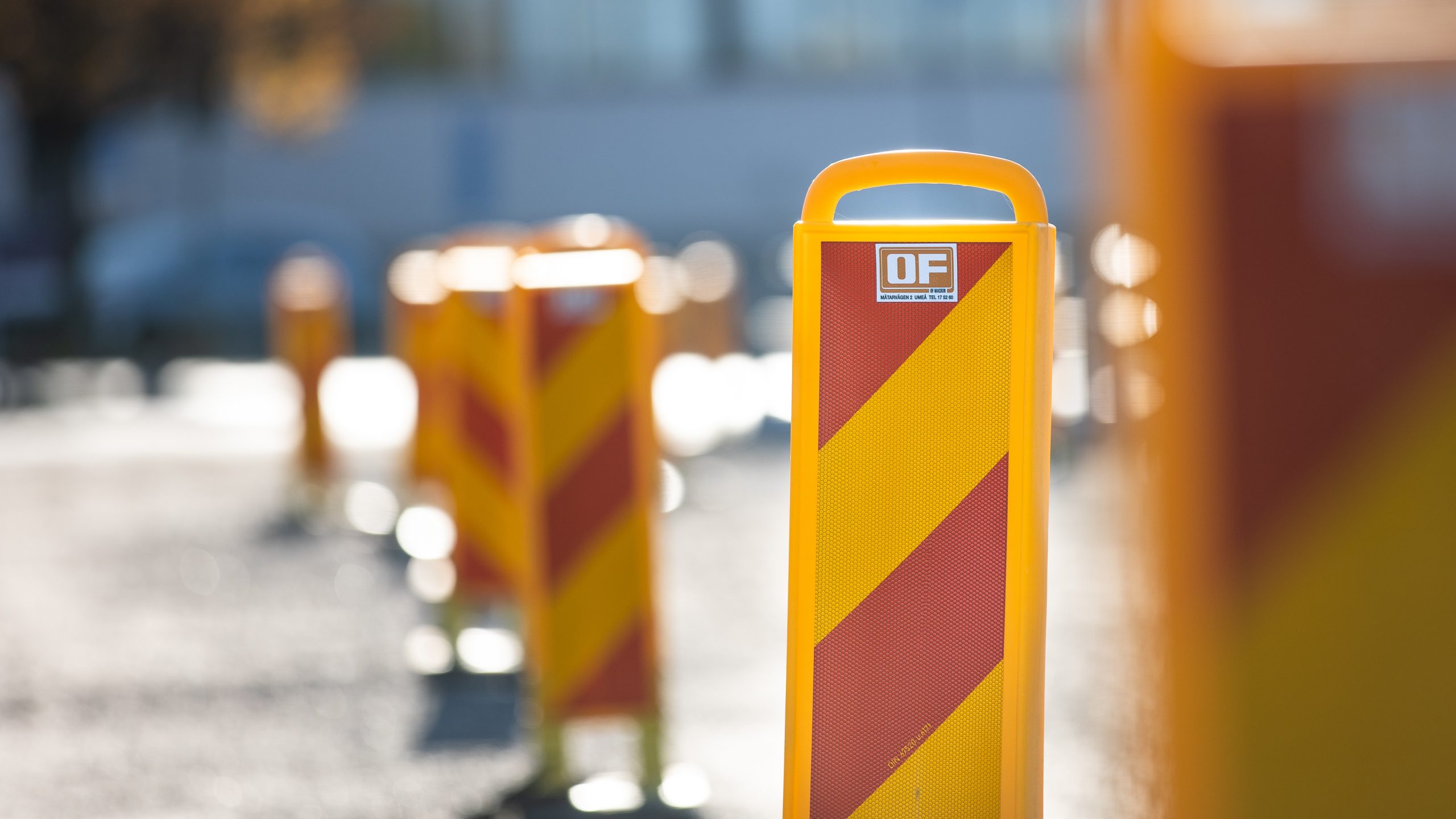 En rad gula och röda trafikanordningar från OF Maskin, uppställda på en solbelyst väg.